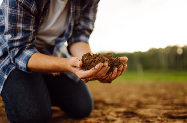 A person kneeling on a farm field analyzing soil quality  in a rural landscape. Garden field ground fertile concept.