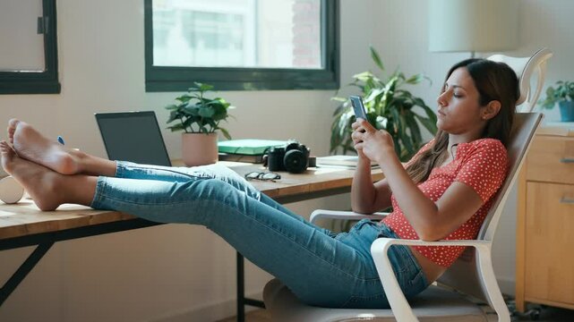 Businesswoman sitting at desk with feet up reading text messages