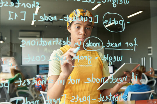 Waist up portrait of Black woman writing computer programming code on glass wall