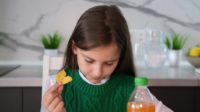 Girl eats potato chips and drinks soda while sitting at table. Concept of unhealthy eating and lifestyle, accumulation of excess weight. Childhood obesity concept.