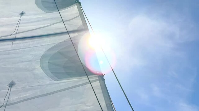 Sun shining through a sailboat mainsail with stitch, rigging, furl, reef, and rope line at sea in the wind