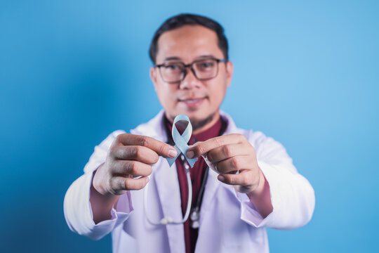 Asian Doctor Holding Light Blue Ribbon For Diabetes and Prostate Cancer Awareness.