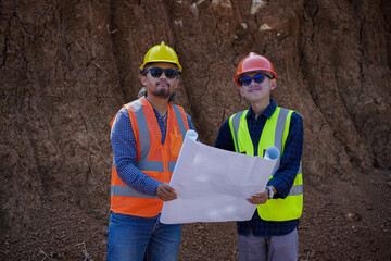 Two young male construction workers are surveying using blueprints in the field