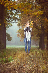 Woman in a leather jacket covers face with hands in autumn misty forest, play hide and seek