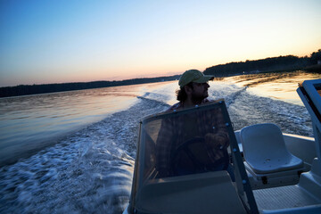 a man driving a boat on the river in the evening at sunset
