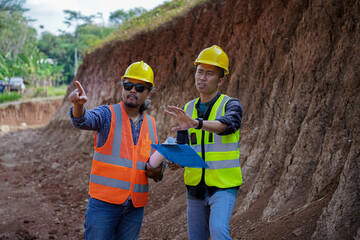 Two young male construction workers are surveying using blueprints in the field