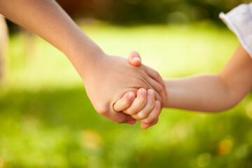 Small children holding hands, close up brother and sister. Not indoors on a sunny, summerday.