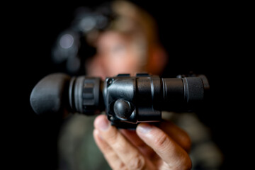 A special forces soldier iwith a night vision device in hand on a black background.