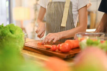 Young woman chopping tomatoes on a wooden cutting board preparing healthy meal in kitchen