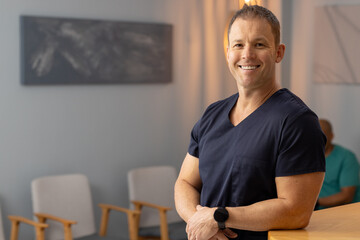 Smiling male doctor, healthcare worker in scrubs in medical clinic, waiting for patients, copy space