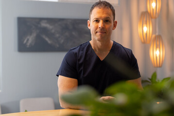Male doctor or healthcare worker in scrubs sitting in medical clinic, smiling and looking at camera