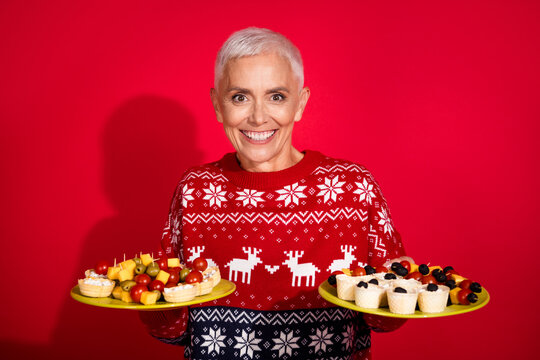 Photo portrait of lovely pensioner lady hold plates snacks party wear print sweater celebrating new year isolated red color background