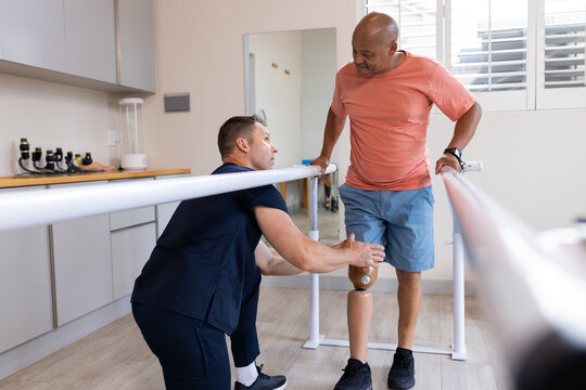 Therapist assisting man with prosthetic leg walking on parallel bars