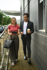 Smiling young business colleagues walking outside near office building and talking