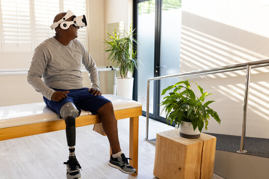 Man with prosthetic leg sitting on bench, using VR headset in rehabilitation center - Powered by Adobe