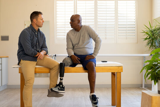 Discussing prosthetic leg, two men sitting on table in medical clinic setting