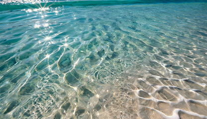 Naklejka premium Crystal-clear turquoise water gently ripples over a sandy beach, reflecting sunlight and creating a peaceful, tropical atmosphere.