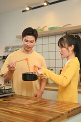 Happy young couple holding a pot with freshly cooked instant noodles, enjoying a casual meal together in kitchen.