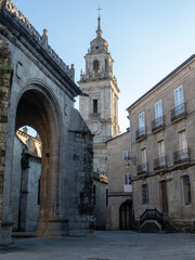 Obraz premium Historic stone archway leading to a tall church tower of the cathedral in Lugo, Spain, under clear blue skies