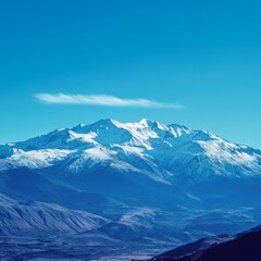 A snow-capped mountain range with a blue sky and a wisp of cloud above.