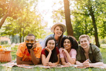 Group of five young and diverse friends lying on blanket having fun in the park