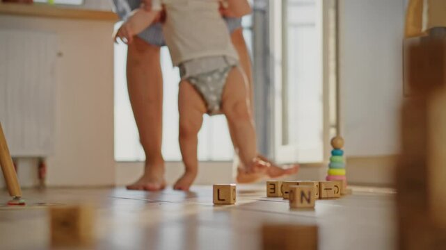 Teaching the first steps a gentle mother accompanies her child. She carefully guides her child's movements, holding his palms. The baby's tiny feet move uncertainly across the surface