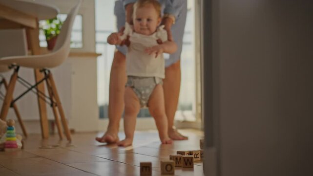 The process of learning to walk a young mother leads her child. The baby's tiny feet tread uncertainly on the floor. She gently holds her child's hands, guiding his movements
