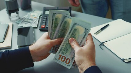 Two individuals conduct a cash transaction at a desk with a calculator and notepad in a modern office setting