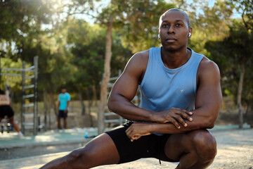 African athletic man dressed in sleeveless blue shirt, black shorts do leg stretch or warming up...