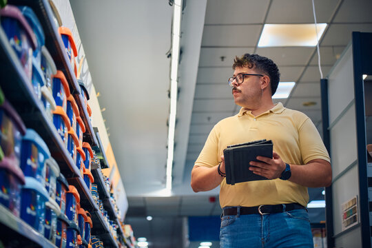 Employee examining products in a retail store aisle while taking notes during the day
