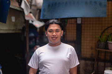 A young Filipino man smiling, standing behind a slum area. A resident of a marginalized squatter...