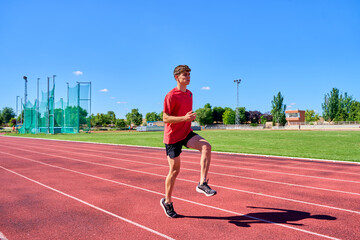 Young male sprinter performing warm-up drills on a track under a clear blue sky