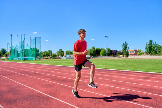 Young male sprinter performing warm-up drills on a track under a clear blue sky