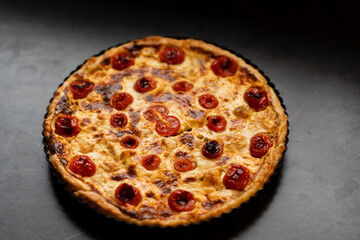 Pie Quiche Lorraine with tomatoes and melted cheese on the table close-up. Copy space.