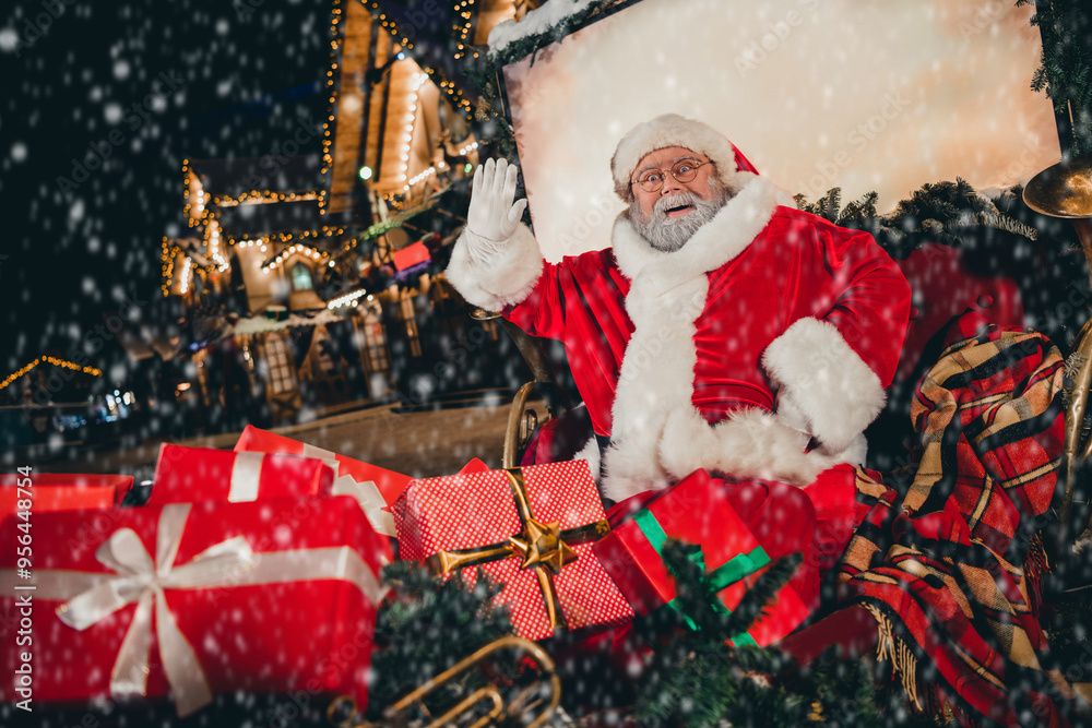 Wall mural Photo of positive bearded santa claus sit sleigh raise hand wave palm congratulate hello sign carry gift good children snowy city outside