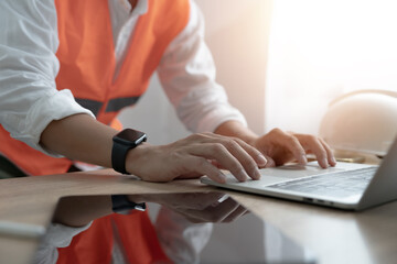 A construction worker is typing on a laptop while wearing an orange safety vest. Concept of...