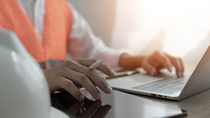 A construction worker is typing on a laptop while holding a pen. Concept of productivity and focus, as the worker is likely working on a project or report related to their job