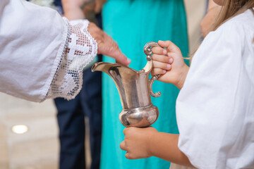 Little girl holding a jug with holy water during baptism ceremony.