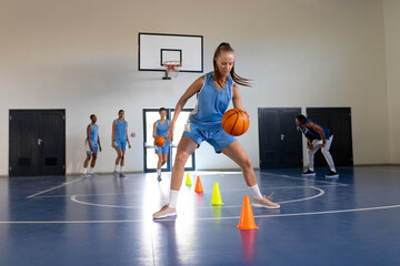 Dribbling basketball around cones, female athlete training in indoor gym