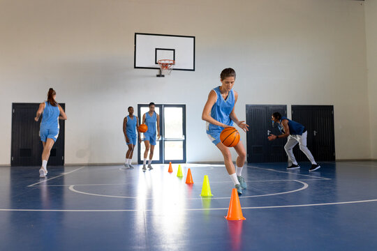 Dribbling basketball around cones, female athlete training in school gym, copy space