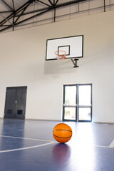 Obraz premium Basketball on court in gymnasium with hoop in background, ready for game, copy space