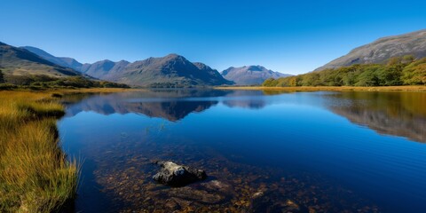 Fototapeta premium A tranquil lake nestled between majestic mountains, reflecting the clear blue sky above, creating a serene ambiance in a picturesque natural landscape.