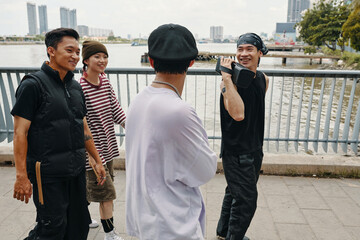 Group of friends smiling and chatting while taking leisurely walk along urban waterfront area with high-rise buildings in the background creating lively atmosphere