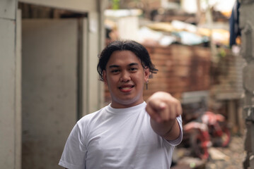 A young Filipino man pointing at the camera. A local person living in an squatter area. Slum area background.