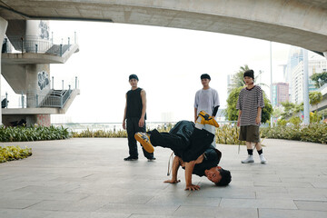 Group of young men practicing breakdance under a large urban bridge, with one in mid-move upside...