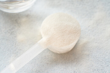 Collagen powder in a plastic measuring spoon with a glass of water on bright background