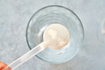 Collagen powder in a plastic measuring spoon above a glass of water, top view