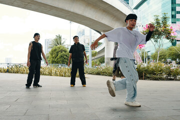 Group of young men performing street dance moves in urban environment with modern architecture and trees in background. Energetic and expressive movement showcasing contemporary dance styles