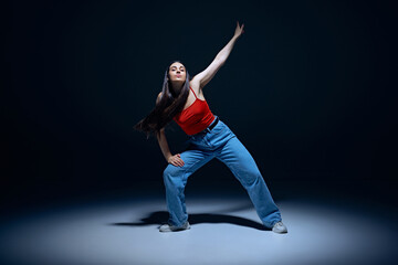 Urban lifestyle. Energetic young woman in jeans and red top performing, dancing hip-hop against black studio background. Concept of street style, contemporary dance, entertainment