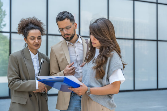 Three diverse business people working and talking focused and thoughtful seriously outside office building, male and female, discussing plans and work project. Businessman and businesswoman teamwork.